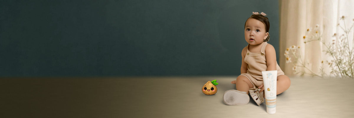 Baby sitting on a cream cushion with a Science Baby skincare tube and a coconut rattle toy.